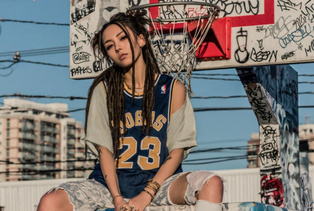 Asian woman with dreadlocks sitting atop a basketball hoop